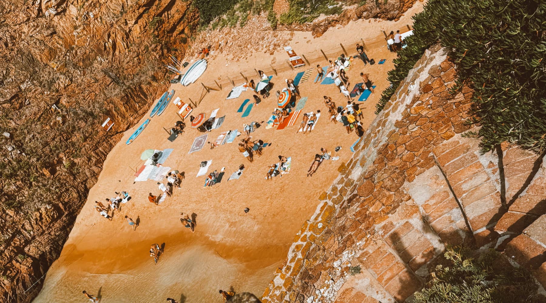 Looking down a cliff path at a busy beach cove in Portugal